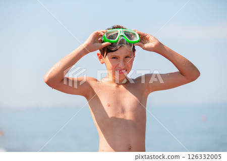 A teenage boy in swimming goggles put his hands behind his head and admires the sea. 126332005