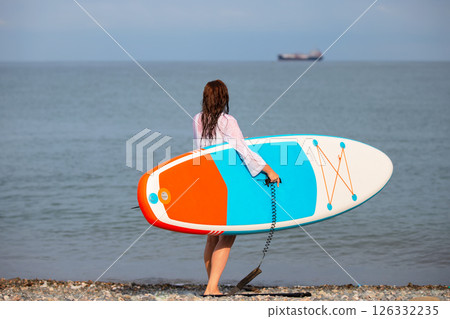 A woman walks along the beach holding a blue boat for sap boarding. A woman enjoys her time on the beach 126332235