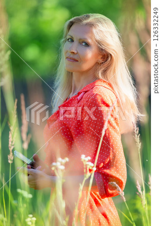 Vertical portrait of a beautiful middle-aged blonde woman among green grass Vertical portrait of a beautiful middle-aged blonde woman among green grass 126332249