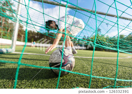 A soccer ball lies in a net on a field. Football is a sport. The concept of scoring a goal. 126332391