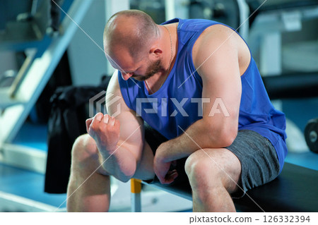 Athletic man looking at his biceps against the background of a gym. 126332394