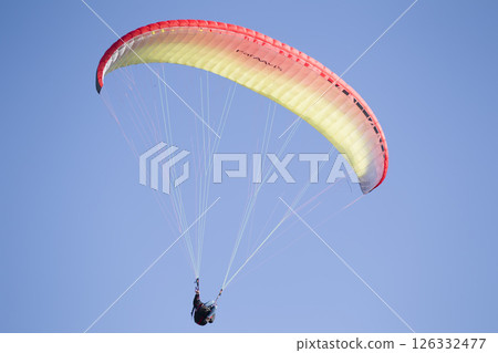 A paraglider flies in the sky under a multi-colored paraglider.Man under parachute 126332477