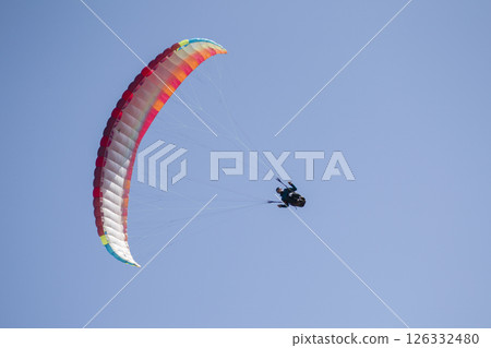 A paraglider flies in the sky under a multi-colored paraglider.Man under parachute A paraglider flies in the sky under a multi-colored paraglider.Man under parachute 126332480