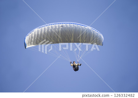 A paraglider flies in the sky under a multi-colored paraglider.Man under parachute 126332482