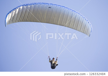A paraglider flies in the sky under a multi-colored paraglider.Man under parachute 126332484