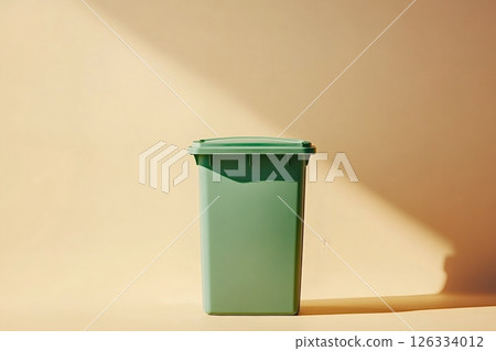 Green wheelie bin standing on beige background in sunlight 126334012