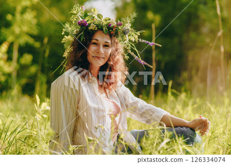 Woman resting in sunny nature with flower crown, fully unplugged and present. Celebration of tradition, simplicity and seasonal beauty 126334074