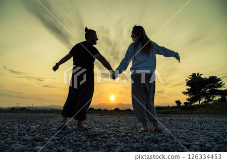 Couple holding hands enjoying sunset on rocky beach 126334453