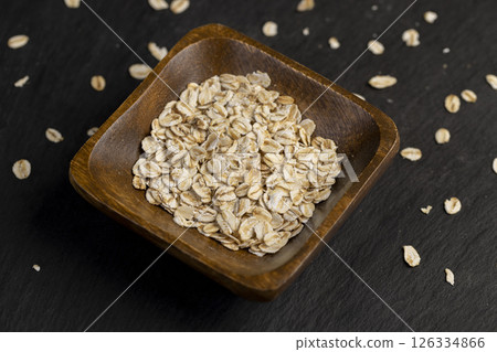 oat flakes poured into a square-shaped wooden bowl, oatmeal for quick cooking of porridge 126334866