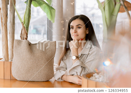 Woman relaxing in cozy cafe with natural decor, wearing elegant watch and linen outfit. 126334955