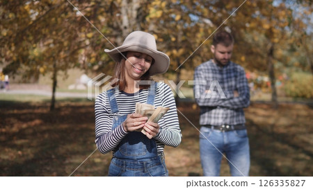 A woman happily counts her cash in a vibrant outdoor setting, surrounded by colorful autumn leaves all around her 126335827