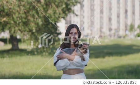A joyful woman holding her cute cat while enjoying a serene day in a peaceful park with an urban backdrop A joyful woman holding her cute cat while enjoying a serene day in a peaceful park with an urban backdrop 126335853