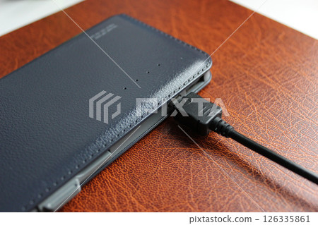 Elegant Leather Trimmed Power Bank Charging On Brown Leather Paper Folder Detailed Stock Photo Elegant Leather Trimmed Power Bank Charging On Brown Leather Paper Folder Detailed Stock Photo 126335861