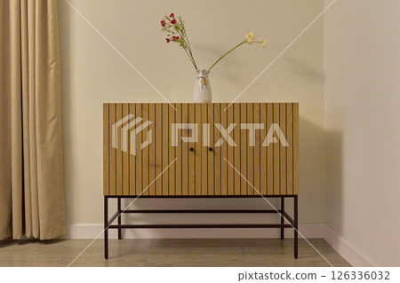 Stylish wooden cabinet displayed against a light wall with flowers 126336032