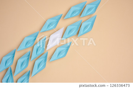 A white origami paper boat stands apart from a group of blue ones, symbolizing uniqueness or leadership, against a neutral background. A white origami paper boat stands apart from a group of blue ones, symbolizing uniqueness or leadership, against a neutral background. 126336473