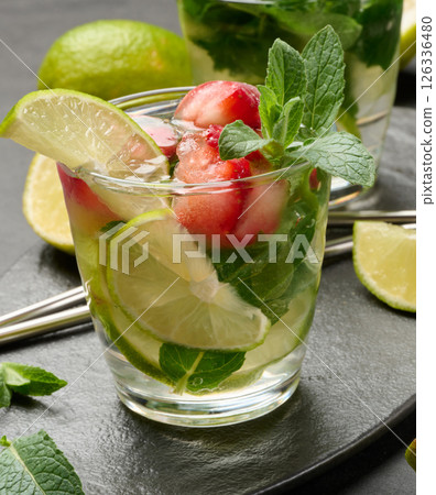 Refreshing mojito cocktail with lime, mint, strawberry, and ice on dark background 126336480