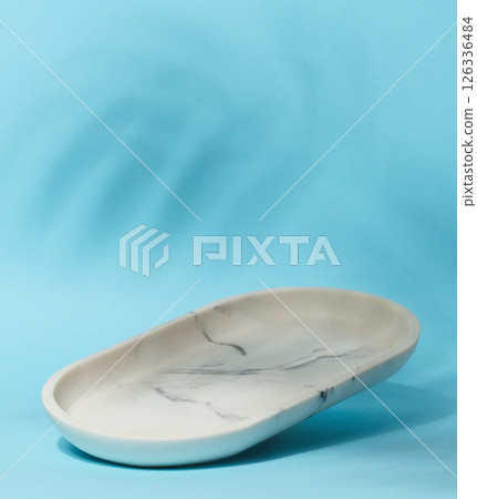 An empty, oval shaped soap dish made of white marble with gray veining sits on a light blue background An empty, oval shaped soap dish made of white marble with gray veining sits on a light blue background 126336484