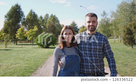 A joyful couple is enjoying a beautiful sunny day at the park, embracing each other and smiling brightly for the camera 126336522