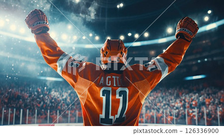 A triumphant hockey player in an orange uniform raises his arms in victory under bright arena lights, celebrating a powerful, emotional sports moment in front of a cheering crowd 126336900