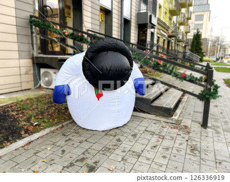Broken life-sized snowman mascot decorates city center during Christmas season. Image with humor. Broken snowman illustrating poor Christmas and winter without snow. Broken life-sized snowman mascot decorates city center during Christmas season. Image with humor. Broken snowman illustrating poor Christmas and winter without snow. 126336919