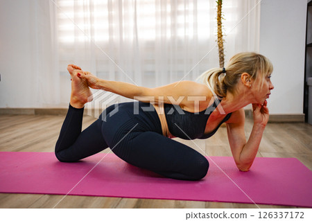 Yoga practitioner performs a deep stretch on a pink mat indoors Yoga practitioner performs a deep stretch on a pink mat indoors 126337172