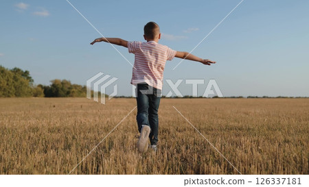 boy child running across field playing airplane flight dream, boy arm wings, imagination play outside, dreamy child game, outdoor child fun, running boy dream, pretend pilot child, energetic kid 126337181