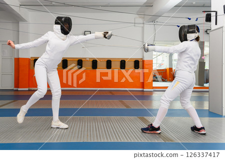 Female fencer leaping forward in attack during indoor match. Female fencer leaping forward in attack during indoor match. 126337417