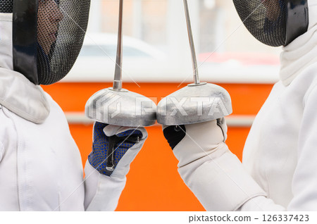 Close-up of female fencers crossing epees before match indoors. Close-up of female fencers crossing epees before match indoors. 126337423