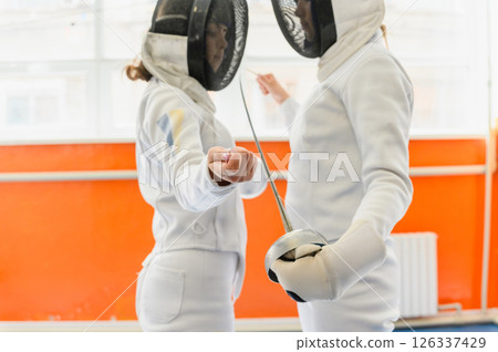 Female fencers touching tips before match in bright hall. Female fencers touching tips before match in bright hall. 126337429