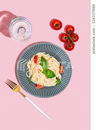 Creamy spaghetti with tomatoes, cheese and basil on a plate on a pink background 126337666