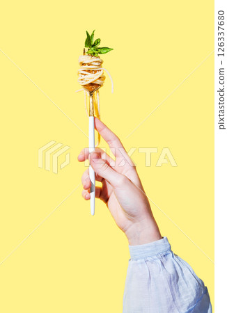 Hand holding fork with creamy spaghetti and basil on isolated bright yellow background. 126337680