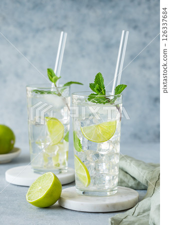 Two glasses mojito cocktail with fresh lime, mint and ice on a marble stand on blue background. 126337684