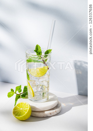 Mojito cocktail in a glass with lime, mint, ice and tube on a marble stand on a light background Mojito cocktail in a glass with lime, mint, ice and tube on a marble stand on a light background 126337686