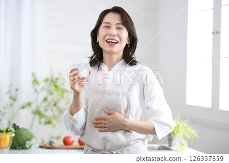Smiling middle-aged woman drinking water in the kitchen 126337859