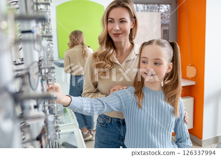 Mom and daughter choosing new eyeglasses in optic shop and looking involved 126337994