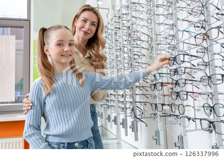 Mom and daughter choosing new eyeglasses in optic shop and looking involved 126337996