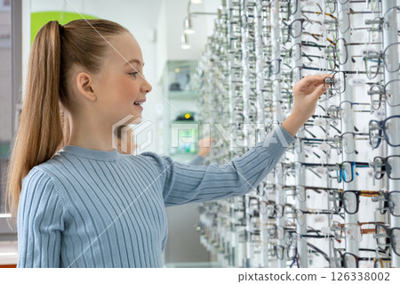 Long-haired caucasian girl choosing new eyeglasses in an optic shop 126338002