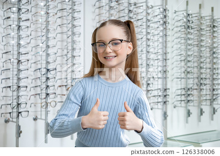 Cute school age girl with long-hair looking contented after choosing new eyeglasses Cute school age girl with long-hair looking contented after choosing new eyeglasses 126338006