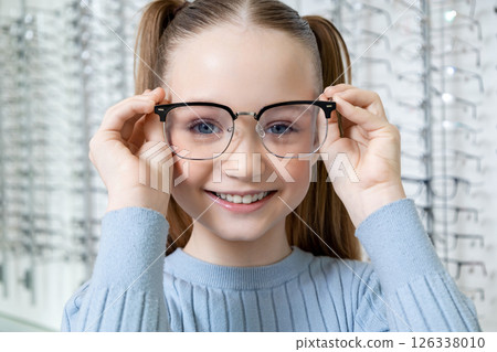 Cute school age girl with long-hair looking contented after choosing new eyeglasses 126338010
