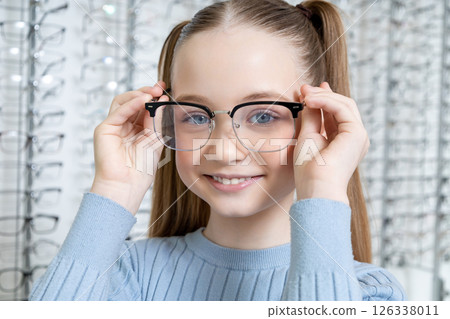 Cute school age girl with long-hair looking contented after choosing new eyeglasses Cute school age girl with long-hair looking contented after choosing new eyeglasses 126338011