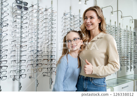 Mom and daughter in optic shop looking positive after choosing new eyeglasses Mom and daughter in optic shop looking positive after choosing new eyeglasses 126338012