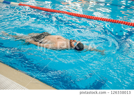 Man in black swimming cap swimming backstroke in the pool 126338013