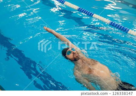 Man in black swimming cap swimming backstroke in the pool 126338147