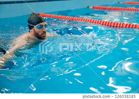 Man in black swimming cap swimming crawl style in the pool Man in black swimming cap swimming crawl style in the pool 126338185