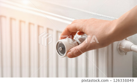 Female hand turns heat meter on gas radiator for heating 126338849