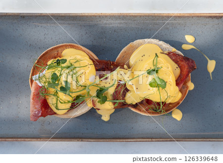 Top view of Eggs Benedict made with english muffin, grilled bacon, a brace of poached hen's eggs & hollandaise sauce and watercress. Top view of Eggs Benedict made with english muffin, grilled bacon, a brace of poached hen's eggs & hollandaise sauce and watercress. 126339648