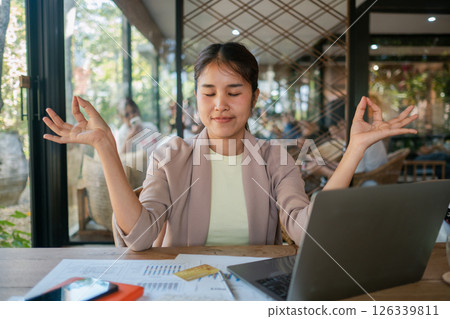 A young professional woman meditating at her desk, promoting mindfulness and stress relief in a contemporary office environment. 126339811