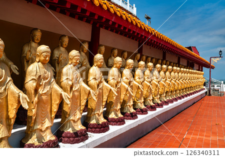 Striking row of golden Buddha statues aligned in front of a traditional red-tiled corridor at Fo Guang Shan Monastery in Kaohsiung, Taiwan. The figures stand in peaceful poses beneath an ornately 126340311