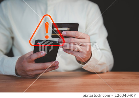 A person holding a credit card and smartphone with a red warning sign overlay, symbolizing online scams, fraud, security risks, and financial caution in digital transactions. 126340407