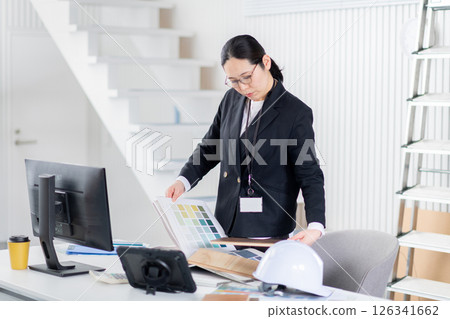 A female employee of a construction company working while spreading out building materials and documents 126341662